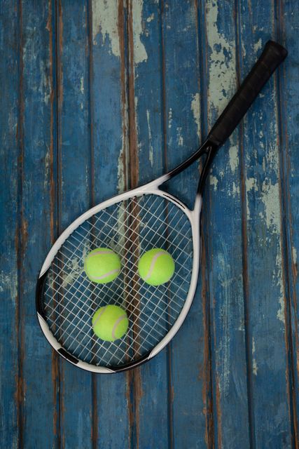 Overhead view of tennis racket and balls on blue wooden table