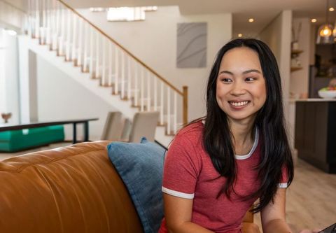 Asian chinese woman smiling on brown leather sofa in modern living room, casual lifestyle