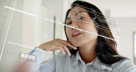 Mid-adult asian woman tilting head and posing with translucent hud data overlay on glass