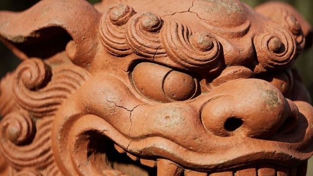 Terracotta guardian lion head sculpture weathering in sunlit garden courtyard detail aged