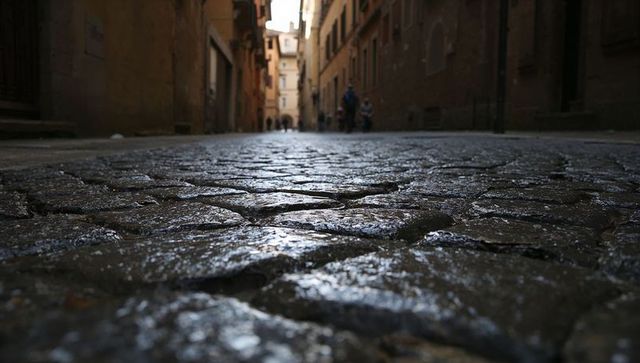 Wet cobblestone alley leading to sunlit archway with blurred pedestrians in distance