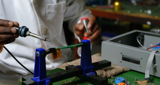 Technician soldering circuit board in electronics workshop, showcasing precision and expertise. Suitable for illustrating technical skills, electronic repair services, or engineering education materials. Can be used in technology blogs, repair service advertisements, or educational content related to electronics and engineering.