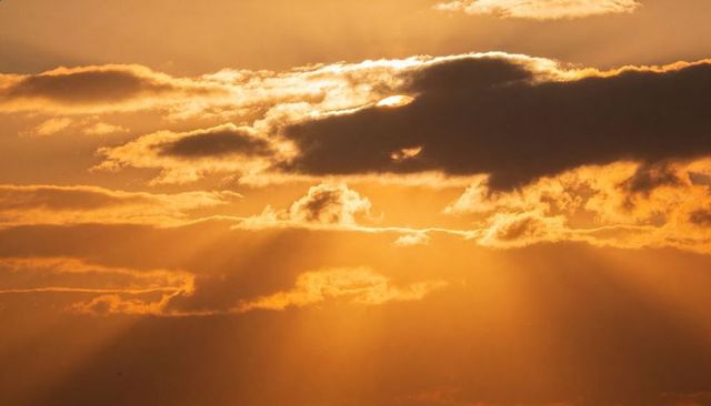 Golden sunrise rays casting through layered clouds, dramatic crepuscular light and warm atmosphere