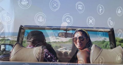 Happy couple driving convertible with tech overlay by the sea