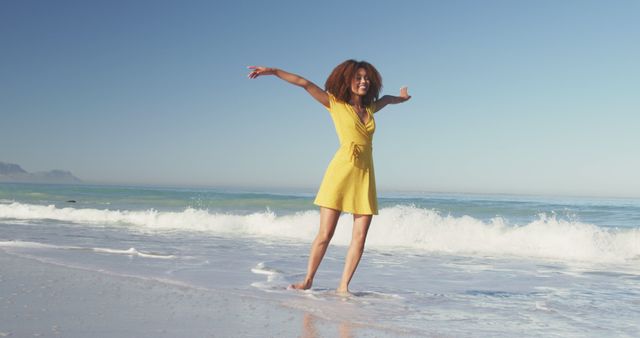 Happy biracial woman dancing on sunny beach by the sea, smiling. Summer, free time, relaxation, freedom and vacations.