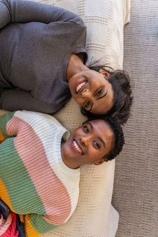 Smiling diverse women relaxing on cream sofa together, cozy friends portrait