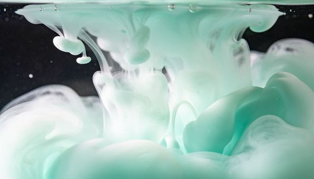 Turquoise and white ink swirling in water creating soft cloud-like plumes macro close-up
