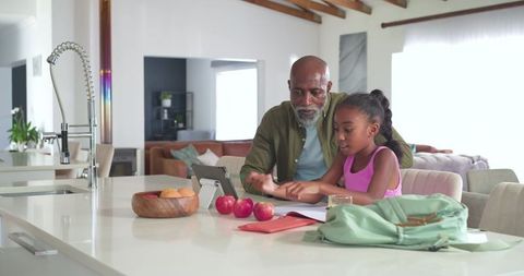 African american grandfather helping daughter with tablet and homework at kitchen island