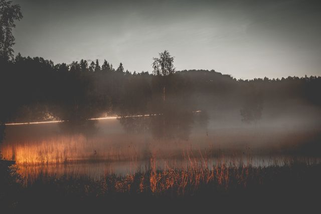 Misty lake illuminated by warm light, creating serene and tranquil atmosphere. Background trees add depth and reflection enhances moodiness. Ideal for use in nature-focused compositions, themed decor, and tranquil scenes.