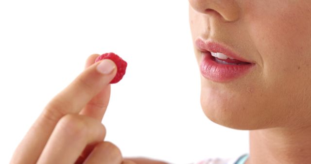 A young Caucasian woman is about to eat a fresh raspberry, with copy space. Her lips are slightly parted in anticipation of the sweet fruit, highlighting a moment of enjoyment.