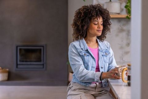 African american woman relaxing at kitchen counter holding mug and french press