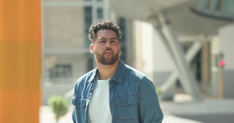 Urban man walking through modern plaza in denim jacket passing orange architectural column