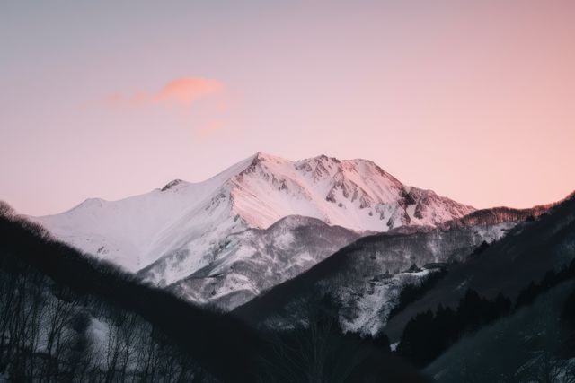 Snow-covered mountains bask in the pink hues of sunset. Serenity envelops the landscape as day transitions to night in this tranquil mountain setting.