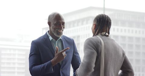 African American Mentor Pointing and Smiling with Young Colleague by Office Window