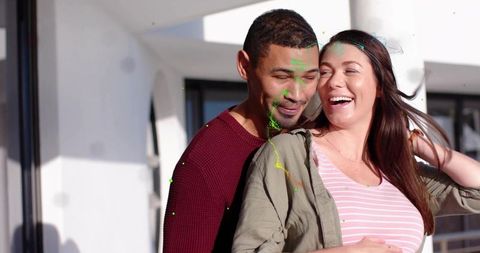 Sunlit balcony embrace: laughing expecting couple sharing joyful moment of modern romance