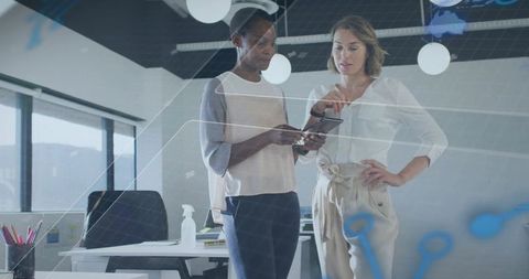 Female colleagues collaborating over tablet in modern office with digital glass overlay