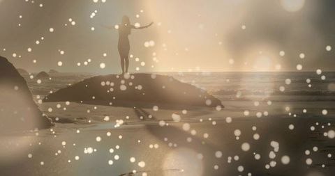Standing woman watching golden sunset from rock on reflective sandy beach with bokeh