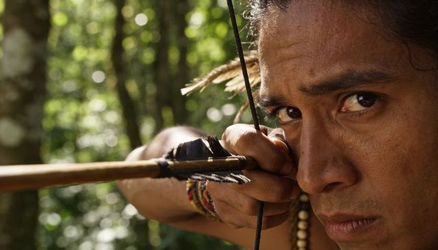 Hispanic archer aiming feathered arrow in sunlit forest closeup, intense focus
