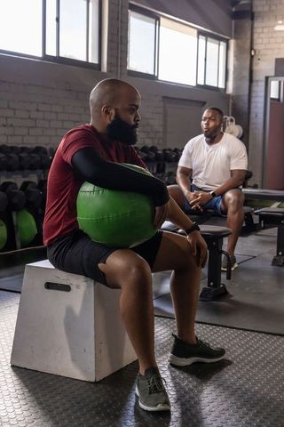 African men resting with green medicine ball on plyo box in industrial gym daylight