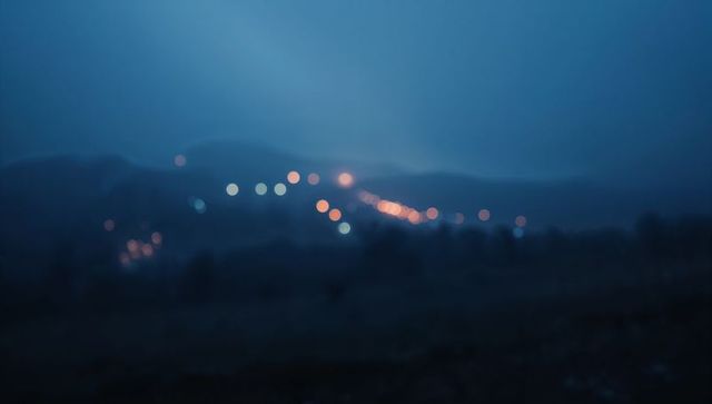 Diagonal bokeh lights stretching across misty distant hills at twilight nightscape