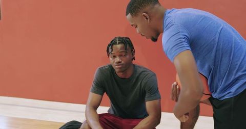 African american coach coaching teen player holding basketball on gym bench during timeout