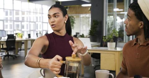 Diverse coworkers sharing coffee and conversation in modern open-plan office breakroom