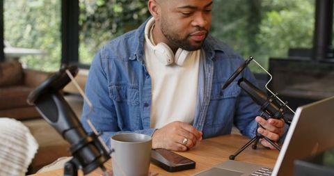African american podcaster adjusting table microphone in home studio monitoring laptop