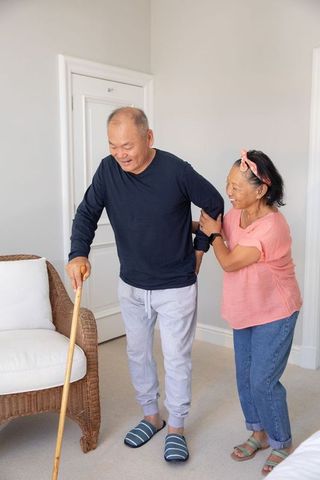 Chinese senior couple practicing home mobility support with cane and gentle companion care