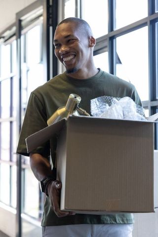 Smiling african american man unpacking brass lamp from moving box in sunlit loft interior