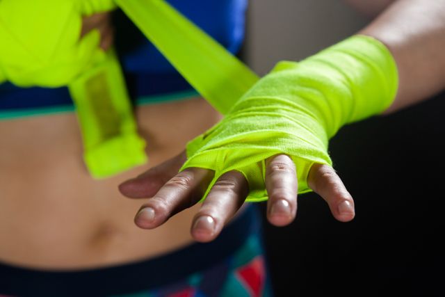 Mid section of woman tying hand wrap on hand in fitness studio
