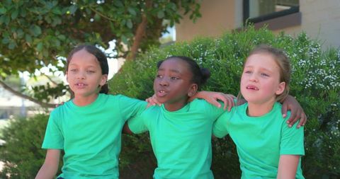 Three girls sitting linking arms wearing matching green t-shirts at school courtyard