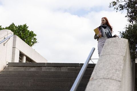 Redhead student standing on campus stairs holding notebook and pink folder