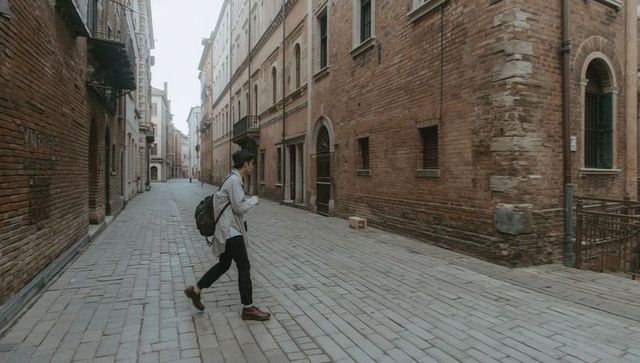 Backpack-wearing traveler walking historic brick alley while checking smartphone
