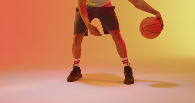 Athlete studiously practicing basketball dribbling set against an orange and yellow gradient background. Ideal for promoting sports events, basketball drills, fitness training programs, and athletic wear brands. Action shot demonstrates skill, dedication, and athletic form in a vibrant, modern setting.