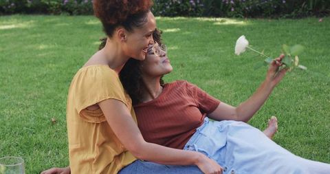 African American Women Embracing on Lawn Holding White Rose, Romantic Outdoor Moment