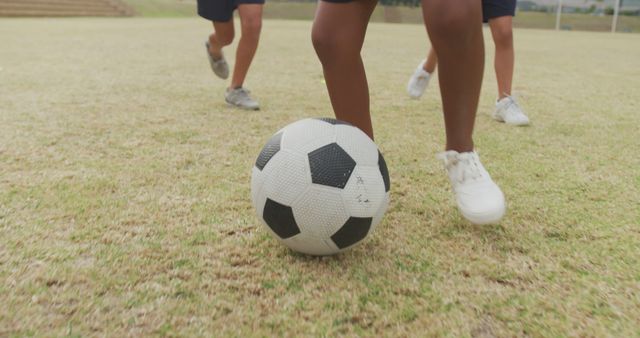 Image of legs of diverse girls playing soccer in front of school. primary school education, sport and exercising concept.