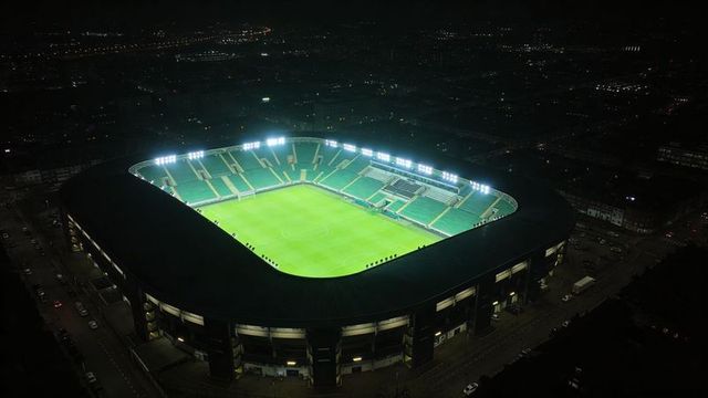 Illuminated football stadium night aerial view empty green pitch floodlights urban
