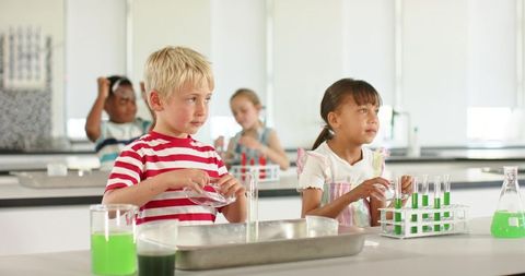 Elementary students mixing bright green solutions in classroom science lab with test tubes