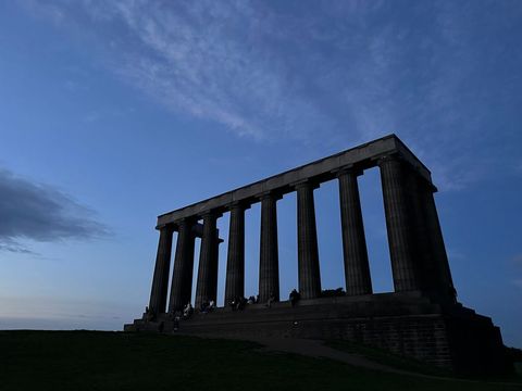 Grand classical-style monument with several large columns set against dramatic evening sky. This landmark stands on Calton Hill, popular destination for tourists visiting Edinburgh. Image ideal for travel brochures, educational materials on architecture, and promotional content for Scottish tourism.