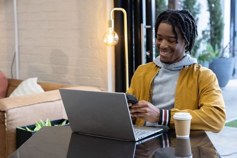 African american man working remotely in cafe using laptop and smartphone with coffee