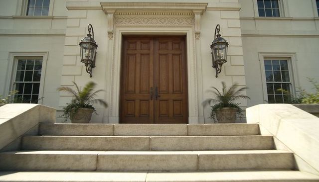 Wooden double doors anchoring neoclassical facade with carved surround, stone steps and lanterns