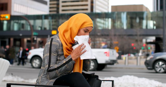 Woman in urban environment sneezing into tissue wearing yellow hijab - Download Free Stock Images Pikwizard.com