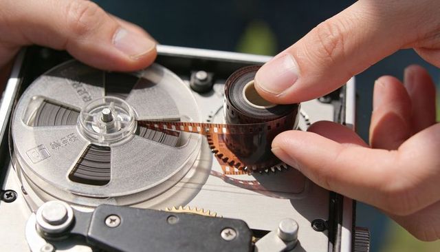 Threading 35mm film onto take-up reel hands guiding film through projector macro sprocket