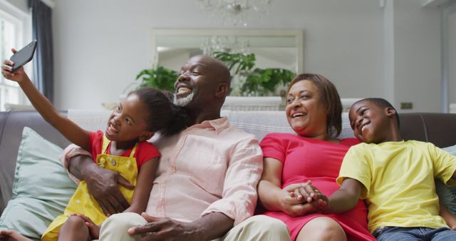 This image captures a loving African American family sitting on a couch, taking a selfie together. Their expressions showcase happiness and togetherness. Perfect for use in advertisements, family-oriented content, health and wellness websites, and social media campaigns promoting family bonding and quality time.