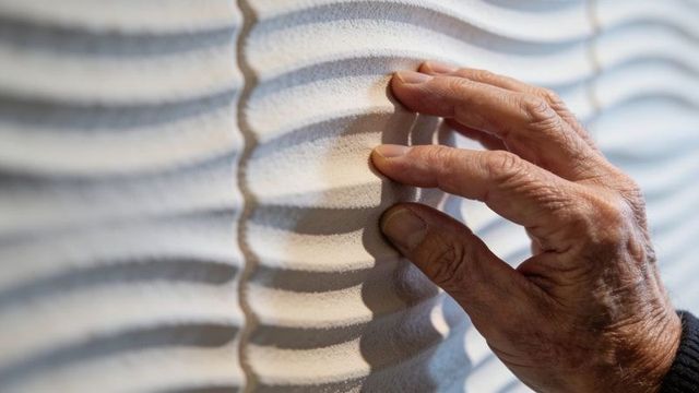 Senior hand tracing wavy textured wall panel close-up emphasizing touch and sensory link