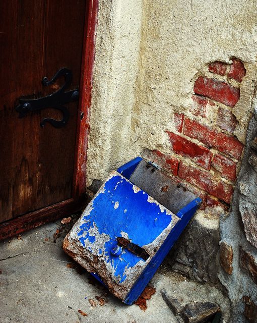 Weathered blue mailbox with peeling paint next to a rustic wooden door on an old brick wall. Image evokes feelings of nostalgia, history, and decay. Great for use in blogs, articles, and projects related to vintage aesthetics, urban decay, and historical preservation.