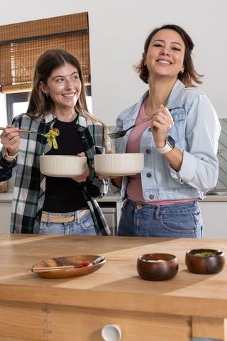 Two friends smiling and enjoying bowls at sunlit kitchen island wearing denim and plaid