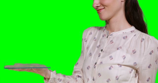 Young woman casually dressed is holding invisible item while smiling. Ideal for tutorials, tech demonstrations, and promotional materials, this easily editable green screen image enables seamless background changes to suit different contexts and messages.
