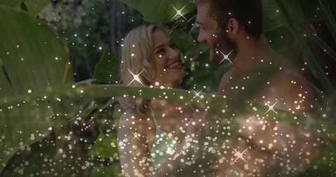 Romantic tropical couple leaning close among lush banana leaves with sparkling bokeh overlay