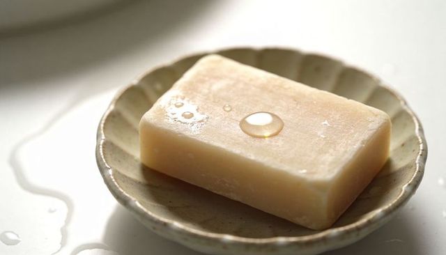 Beige natural soap bar resting on scalloped ceramic dish with water droplets